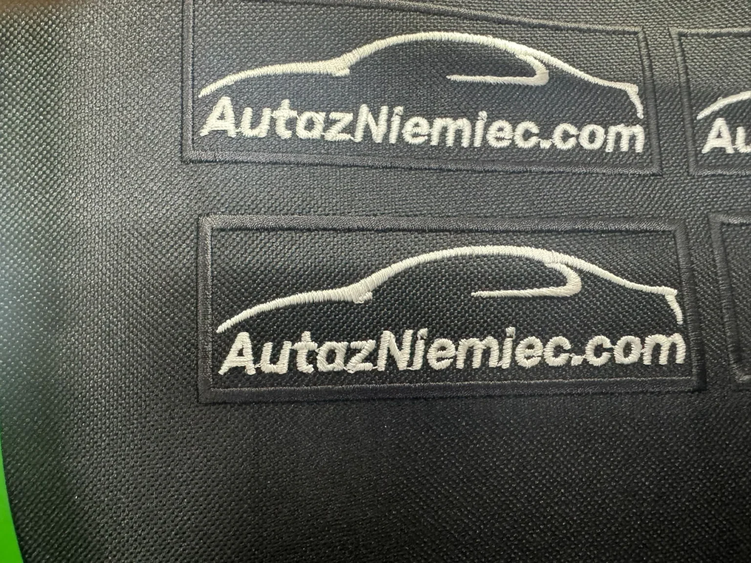 Czarne naszywki haftowane AutozNiemiec.com z motywem samochodu